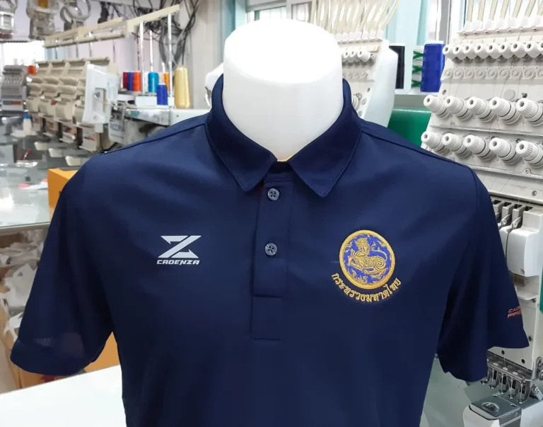 ปักโลโก้ตราสัญลักษณ์สีทองบนเสื้อโปโลสีกรมท่า งานปักจักรคอมพิวเตอร์